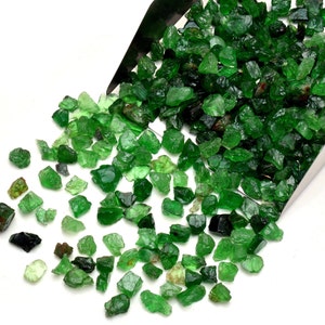 May include: A close-up of a pile of green gemstones, some of which are spilling out of a metal scoop. The gemstones are rough and have a variety of shapes and sizes.