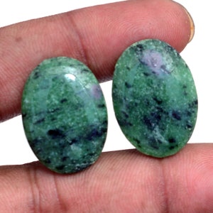 May include: Two oval-shaped green gemstones with black and white inclusions. The stones are smooth and polished.