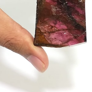 May include: A rough, rectangular, pink and brown gemstone with a natural, faceted finish.
