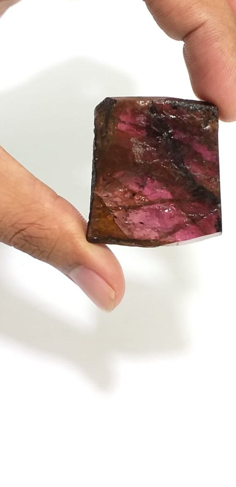 May include: A rough, rectangular, pink and brown gemstone with a natural, faceted finish.