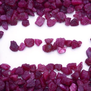 Può includere: Un'immagine ravvicinata di una superficie bianca con un bordo di piccole pietre di rubino rosa. Le pietre di rubino sono disposte in una linea al centro dell'immagine, formando la parola "LOVE".