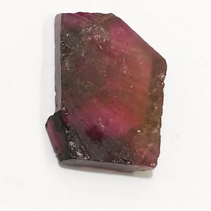 May include: A rough, faceted, pink and green tourmaline gemstone with a dark brown edge.