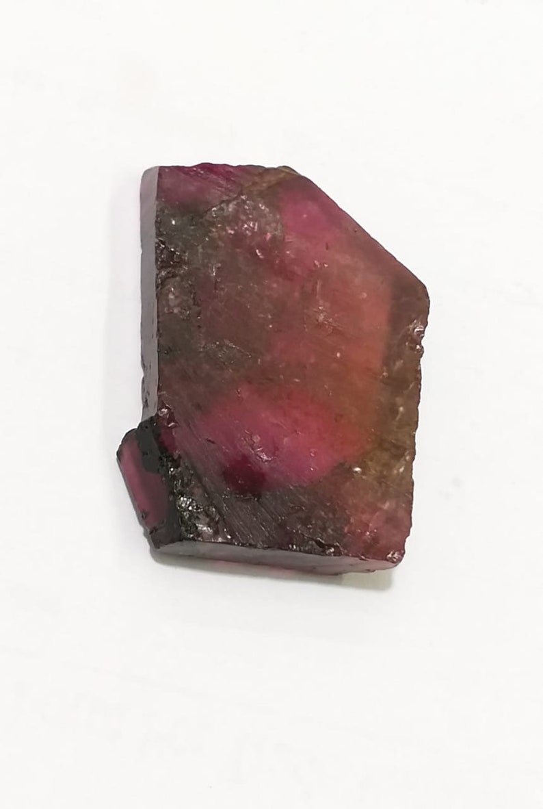 May include: A rough, faceted, pink and green tourmaline gemstone with a dark brown edge.
