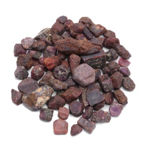 Puede incluir: Un montón de piedras preciosas de rubí rojo en bruto. Las piedras son de varios tamaños y formas, algunas tienen un tono más púrpura.