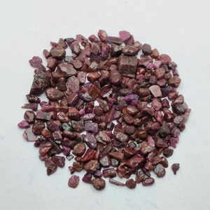 Puede incluir: Un montón grande de pequeñas piedras preciosas de rubí rojo y púrpura sin pulir. Las piedras son de varias formas y tamaños.