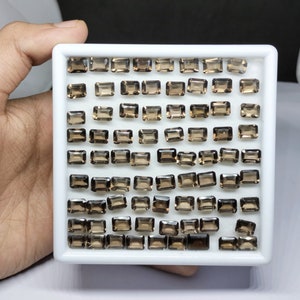 Puede incluir: Una bandeja de 64 piedras preciosas de cuarzo ahumado, cada una cortada en forma rectangular. Las piedras preciosas están dispuestas en un patrón de cuadrícula y todas son aproximadamente del mismo tamaño.