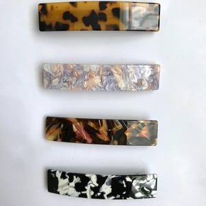 Può includere: Quattro fermagli per capelli con diversi motivi. I fermagli sono realizzati in materiale marrone, bianco, nero e multicolore. I fermagli sono tutti di forma rettangolare e hanno una leggera curvatura.