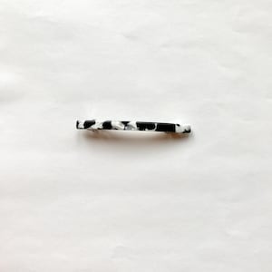May include: A black and white patterned hair clip. The clip is made of plastic and has a smooth, glossy finish.