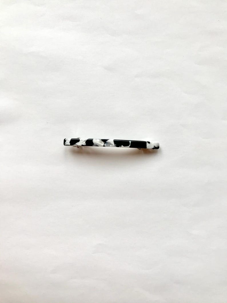 May include: A black and white patterned hair clip. The clip is made of plastic and has a smooth, glossy finish.