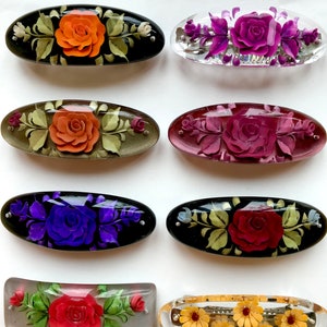 May include: Eight vintage floral hair clips with different coloured flowers and designs. The clips are made of plastic and have a shiny finish. Some of the clips have a black background, while others are clear.