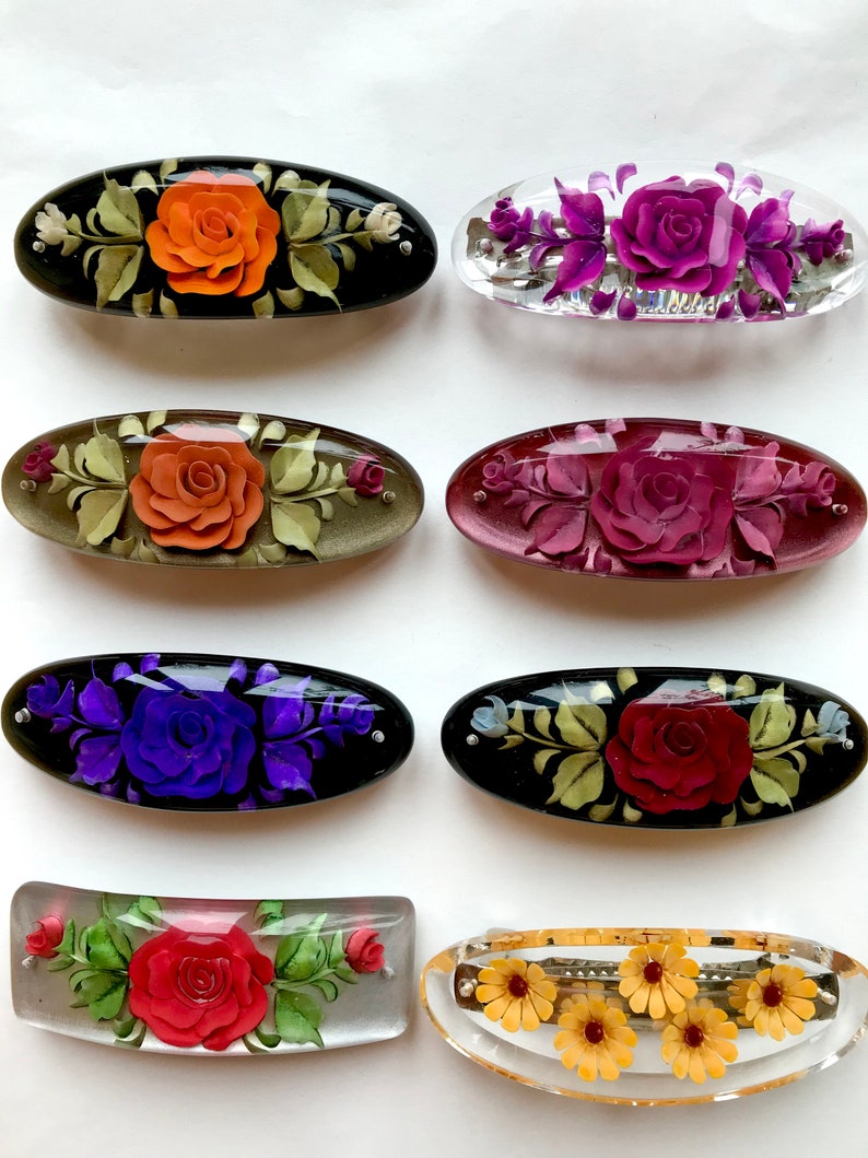 May include: Eight vintage floral hair clips with different coloured flowers and designs. The clips are made of plastic and have a shiny finish. Some of the clips have a black background, while others are clear.