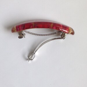 May include: A red and gold hair clip with a curved shape and a metal clasp.