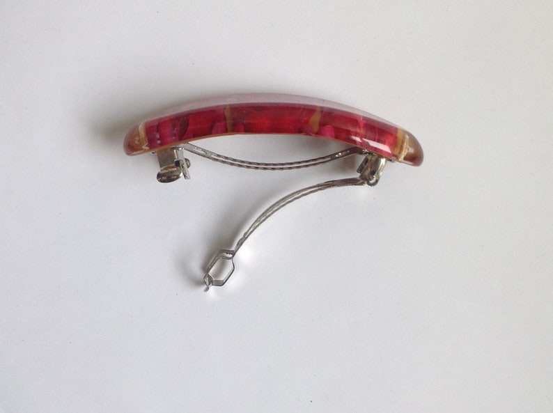 May include: A red and gold hair clip with a curved shape and a metal clasp.