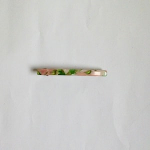 May include: A white, green, and pink hair clip with a marbled pattern.