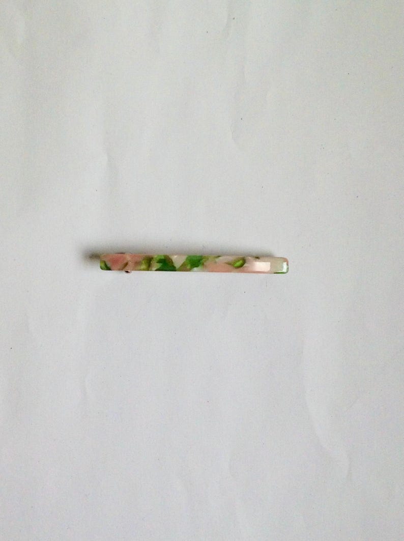 May include: A white, green, and pink hair clip with a marbled pattern.