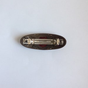 May include: A brown oval hair clip with a silver metal clasp and a red rose design.