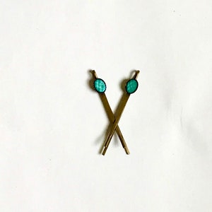 May include: Two gold hair clips with turquoise blue oval-shaped embellishments.
