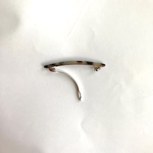 May include: A tortoiseshell hair clip with a silver metal bar and a silver metal clasp.