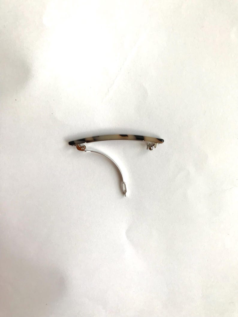 May include: A tortoiseshell hair clip with a silver metal bar and a silver metal clasp.