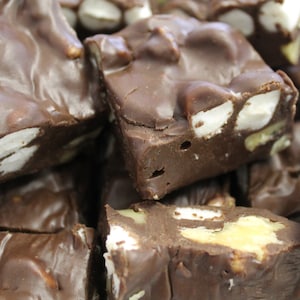 May include: Close-up of a pile of chocolate fudge with marshmallows and nuts. The fudge is a rich brown color and the marshmallows are white. The nuts are a light brown color.