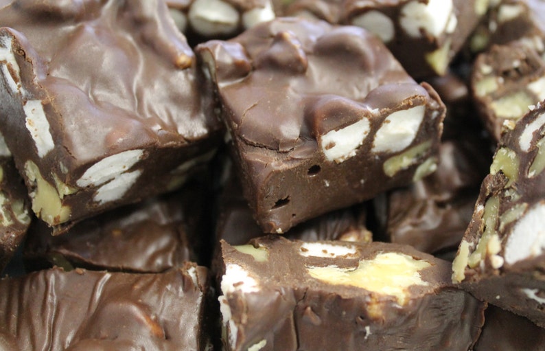 May include: Close-up of a pile of chocolate fudge with marshmallows and nuts. The fudge is a rich brown color and the marshmallows are white. The nuts are a light brown color.