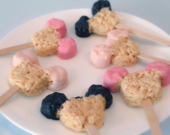 May include: A plate of Mickey Mouse shaped rice crispy treats on sticks. The treats are dipped in pink, white, and black chocolate.