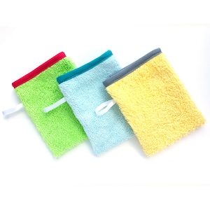 May include: Three colorful washcloths with different colored trim. The washcloths are made of a soft, textured fabric. The washcloths are green, blue, and yellow.
