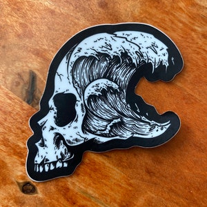 May include: Black and white sticker of a skull with a wave crashing over it. The wave is depicted in a detailed, stylized manner.