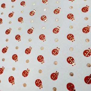 May include: A light blue background covered with red ladybugs and gold flower-shaped embellishments. The ladybugs have black heads and white spots. The gold embellishments are small and scattered.