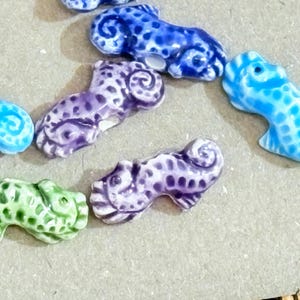 May include: A collection of small, ceramic animal figurines in various colors. The figurines include blue, purple, and green creatures with spotted patterns and curled tails. The details are highlighted with white accents.