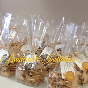 May include: A group of clear plastic bags filled with animal-shaped crackers, tied with twine and decorated with small tags. The tags have a brown and white animal illustration and the text "Fort Lauderdale Invitations".