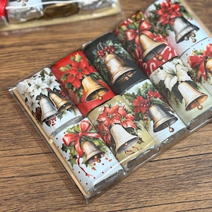 May include: A collection of individually wrapped chocolate bars with festive Christmas-themed designs. Each bar features a bell illustration with poinsettias, bows, and holly. The wrappers are in various colors, including red, white, and black.