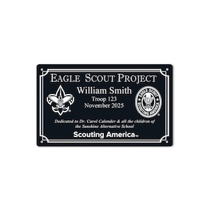 May include: A black rectangular plaque with white text and accents. The text reads "Eagle Scout Project" and includes the name "William Smith", troop number, and date. The plaque features the Boy Scouts of America logo.