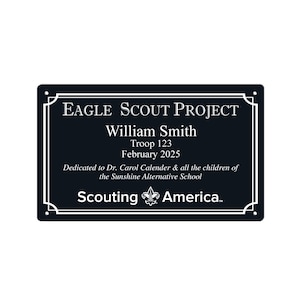 May include: A rectangular black plaque with white text and a white border. The text reads "EAGLE SCOUT PROJECT" and includes the name "William Smith", troop number, and date. The plaque also includes the text "Scouting America."
