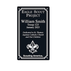May include: A black rectangular plaque with white text and a white border. The text reads "EAGLE SCOUT PROJECT" at the top, followed by "William Smith, Troop 123, January 2025." Below is "Dedicated to St. Thomas Aquinas Catholic Church and Our Children."