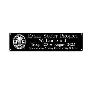 May include: Black rectangular plaque with white text. The plaque features the Eagle Scout emblem and the text "EAGLE SCOUT PROJECT William Smith Troop 123 August 2025 Dedicated to Albany Community School."
