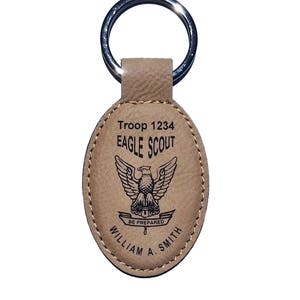 May include: Tan leather Eagle Scout keychain with a silver metal ring. The oval-shaped tag features the text "Troop 1234 EAGLE SCOUT" above an eagle emblem and the words "BE PREPARED" and "WILLIAM A. SMITH".
