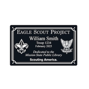 May include: A black rectangular plaque with white text and decorative borders. The text reads "Eagle Scout Project" and includes a name, troop number, and date. The plaque features the Boy Scouts of America emblem.