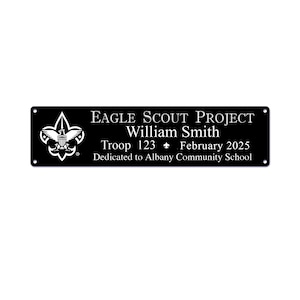 May include: Black rectangular plaque with white text and a Boy Scouts of America emblem. The text reads "EAGLE SCOUT PROJECT William Smith Troop 123 February 2025 Dedicated to Albany Community School."