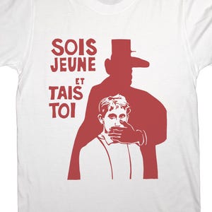 May include: White t-shirt with a red graphic. The graphic features a silhouette of a person covering another person's mouth, with the French text "SOIS JEUNE ET TAIS TOI" above.