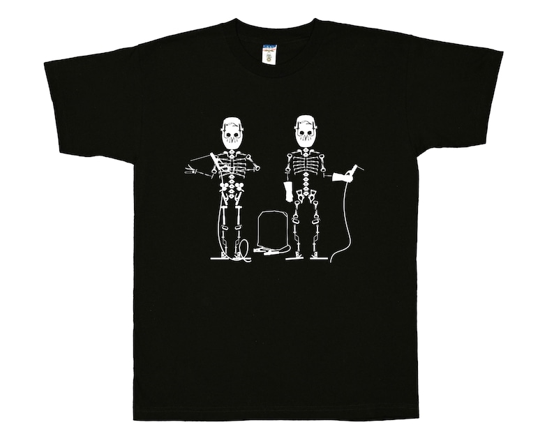May include: A black short-sleeve t-shirt featuring a white graphic print of two skeletons wearing welding helmets. The skeletons are depicted with welding equipment, including a torch and cables, positioned on either side of a welding tank.