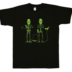 May include: A black short-sleeve t-shirt featuring a bright lime green graphic print of two skeletons wearing welding masks. One skeleton holds a welding torch while the other holds a welding rod, with a rectangular welding tank positioned between them.