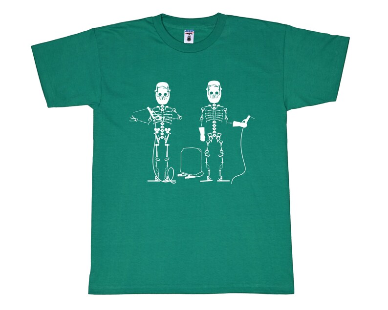 May include: A short-sleeve emerald green t-shirt featuring a white graphic print of two skeletons wearing welding helmets and gloves. The skeletons are depicted holding welding equipment with a central welding tank positioned between them.