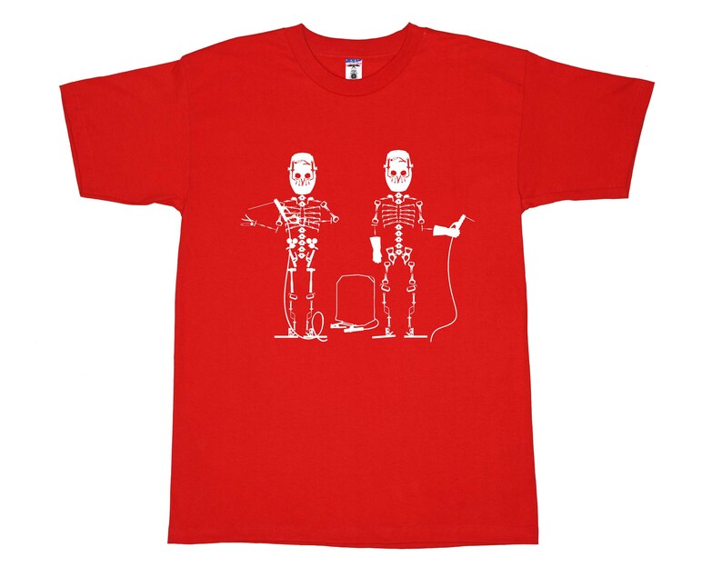 May include: A bright red short-sleeved t-shirt featuring a white graphic print of two skeletons wearing welding helmets. The skeletons are depicted holding welding equipment, with a welding machine positioned between them on the chest area.