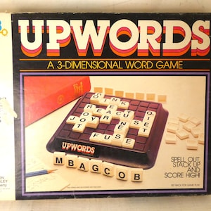 May include: A vintage board game box for Upwords, a 3-dimensional word game. The box is black with red and white lettering. The game is for 2-4 players, ages 10 and up. The box shows a close-up of the game board with letter tiles and the words "Spell out, stack up and score high!"
