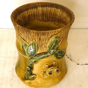 Może przedstawiać: Ceramiczna doniczka z brązową i zieloną glazurą, przedstawiająca wypukły wzór bambusowych łodyg i liści. Na podstawie doniczki znajduje się żaba.