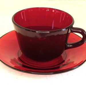 Puede incluir: Un juego de taza y platillo de té de vidrio rojo. La taza y el platillo son de un color rojo intenso y rico.