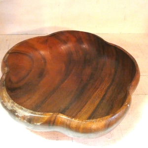 Pode incluir: Uma tigela de madeira com uma borda exclusiva e ondulada. A tigela é feita de madeira marrom escura com padrões de grãos visíveis. O interior é liso e polido, enquanto a borda mostra algum desgaste. Esta tigela decorativa é ideal para servir ou exibir.