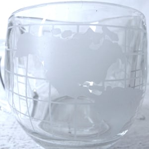 May include: Clear glass mug with a handle, featuring a frosted globe design. The globe design includes latitude and longitude lines. The mug is transparent, allowing the contents to be visible. The mug is part of a set.
