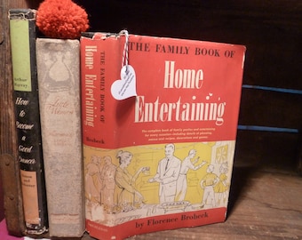 Puede incluir: Un libro rojo, blanco y azul titulado "The Family Book of Home Entertaining" de Florence Brobeck. La portada del libro presenta una ilustración colorida de personas reunidas alrededor de una mesa, disfrutando de una comida.